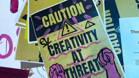 BBC A yellow and purple poster with the words: Caution: Creativity at Threat