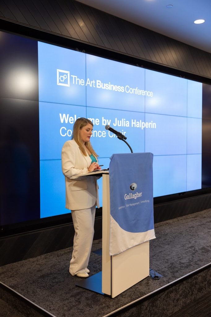 an image of Julia Halperin at the podium in a white suit delivering remarls
