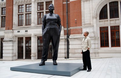 A Black man looking at a tall sculpture of a Black woman.