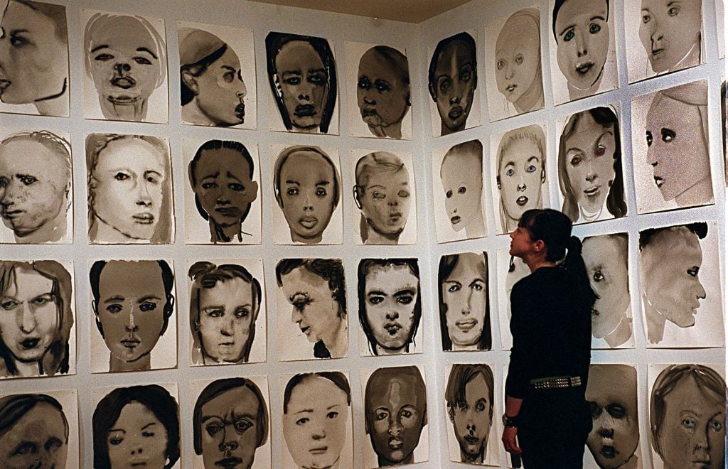 a gallery space that is installed with wall-to-wall black-and-white painted sketches of different women's faces