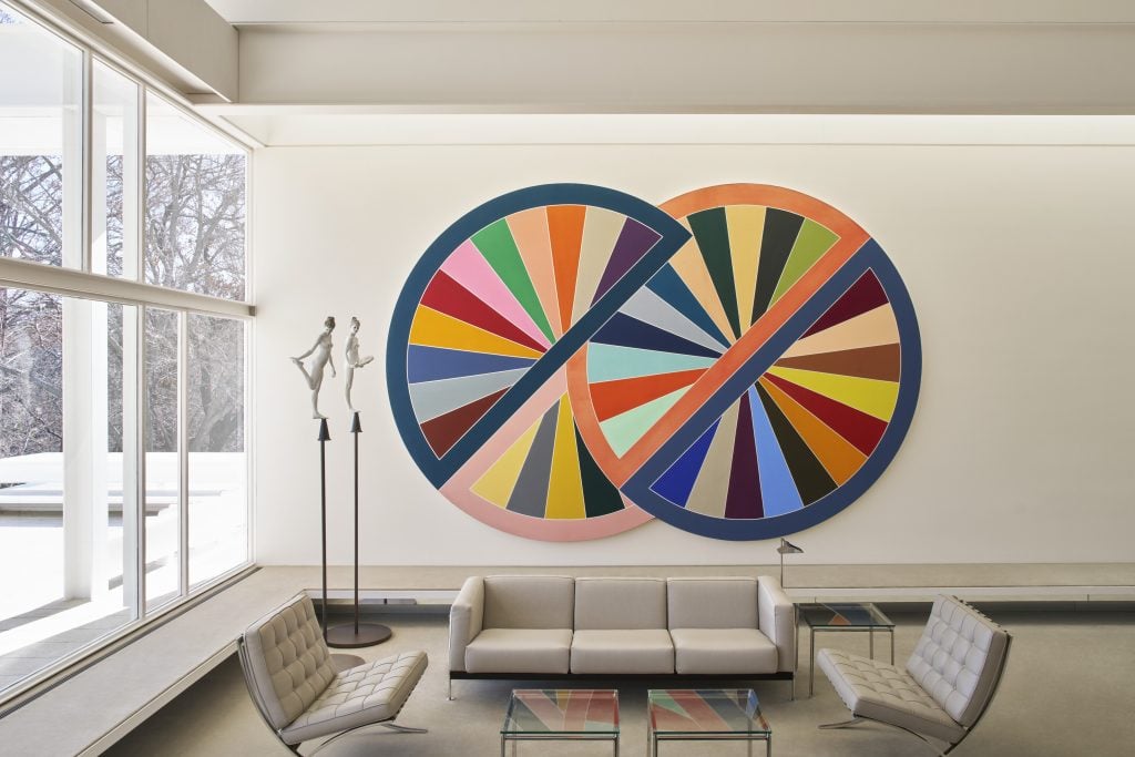 Contemporary living room showcasing a colorful Frank Stella circular painting above modern seating and large windows.