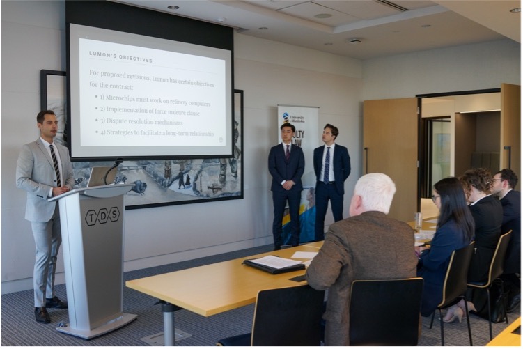 a law student standing behind a podium in a classroom gives a speech to listeners with a presentation projected on a screen next to him.