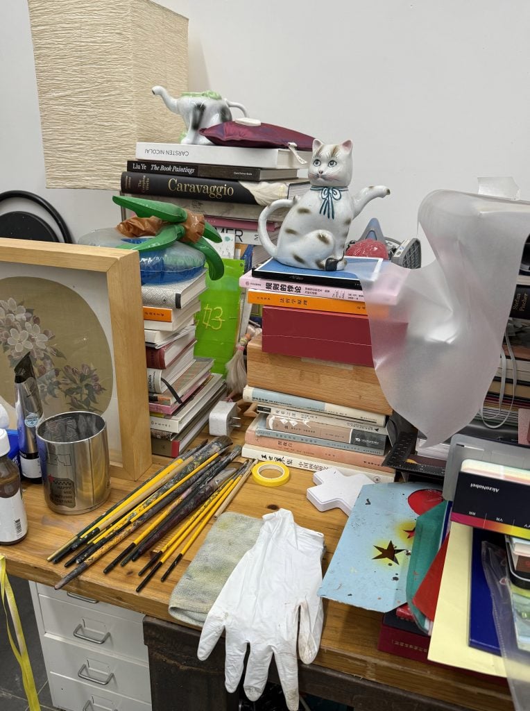 A desk full of books and paint brushes.