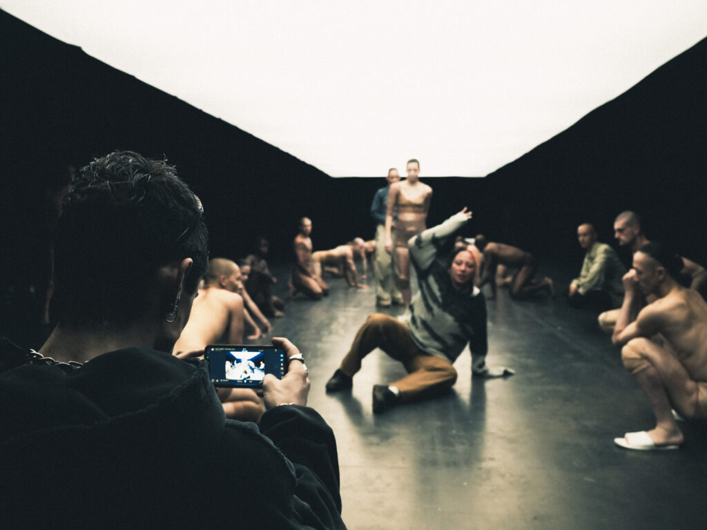 One person holds a phone and records dancers rehearsing on set.