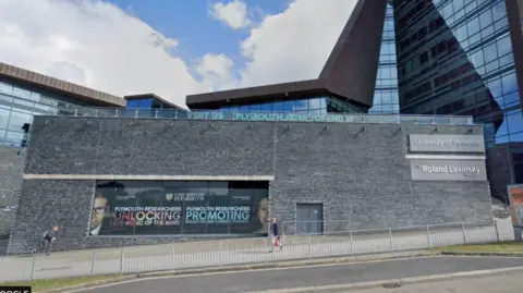Google Two people walk in opposite directions past a grey University of Plymouth building