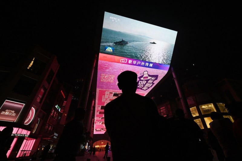 A man watches a news program about Chinese military drills surrounding Taiwan, on a giant screen outside a shopping mall in Beijing on Oct. 14, 2024.