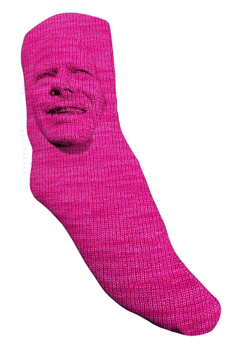 A bright magenta knitted sock sculpted to form the shape of a human head. The face, with realistic contours and expression, appears to be smiling or mid-laugh, creating a surreal and humorous fusion between textile and portraiture.
