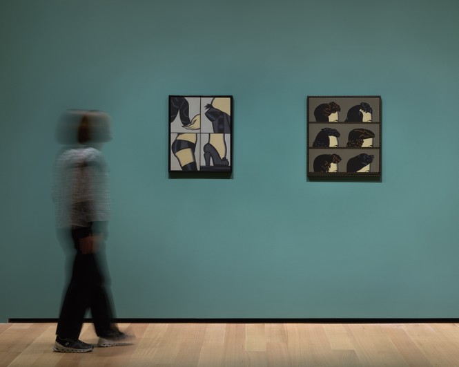 Photo of a woman walking in a gallery setting with two artworks on the wall to her right