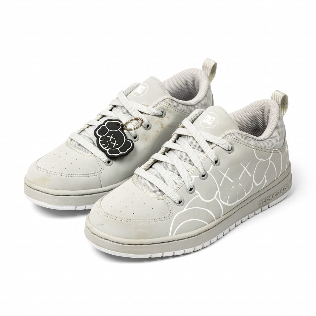 White DC shoes belonging to Pharrell Williams with KAWS Companion face tag and abstract X-eyed character outline graphics.