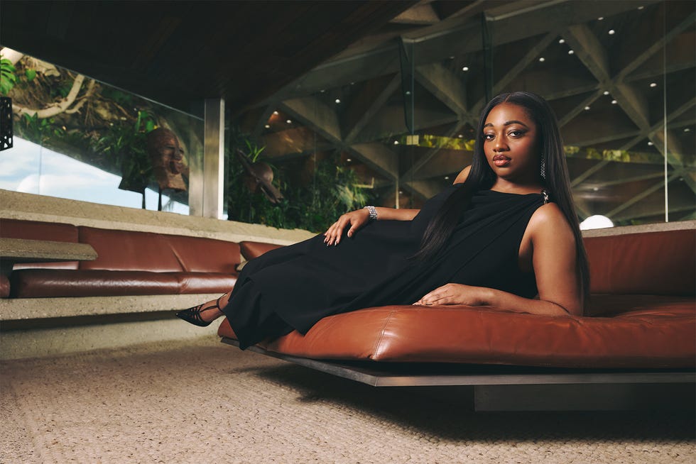 Female figure lounging casually on a brown leather couch in a modern interior