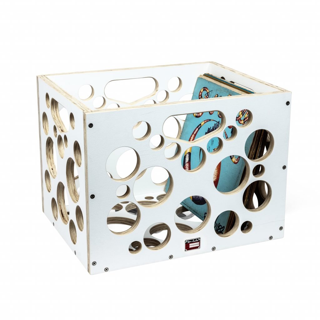 White plywood crate with circular cutouts, filled with vinyl records, against white background.