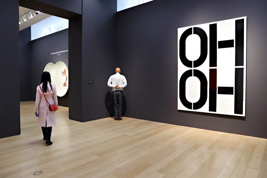 a large text artwork with the words Oh Oh on it next to a sculpture of a man facing the corner of the room