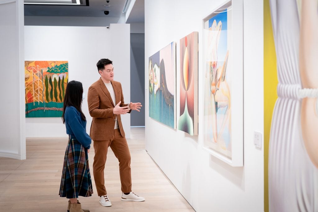 A man and a woman discuss paintings hung on the white walls.
