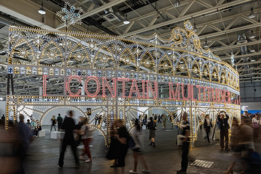 A lot of people at an exhibition of a large scale installation made with a lot of light bulbs.