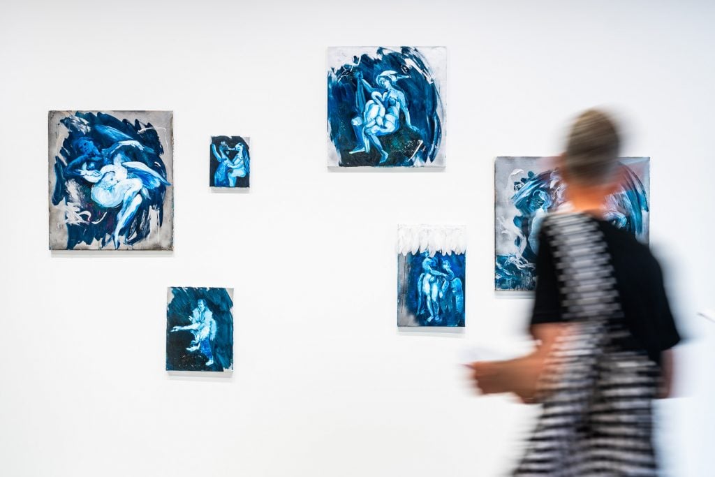 A woman looking at small blue artworks hung on a white wall.