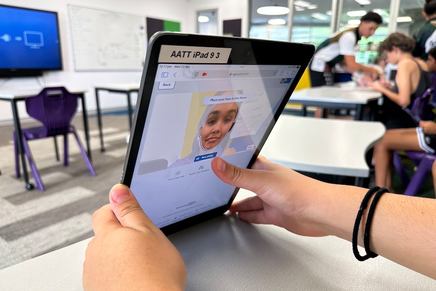 A child's hands hold a tablet in a classroom