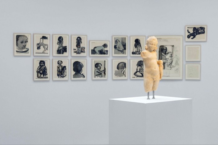 A photograph of an exhibition featuring art work on the wall and a statue on a plinth