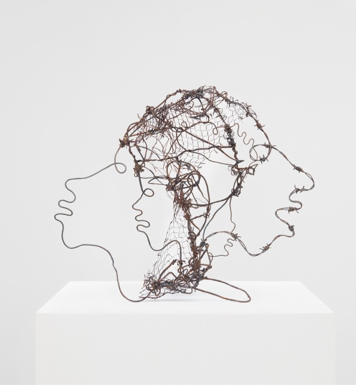 Photograph of a three-dimensional sculpture in which the outlines of two cartoonish heads, facing in opposite directions, are rendered in metal wire